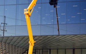 Żółty podnośnik koszowy przy szklanej elewacji zdj. 1